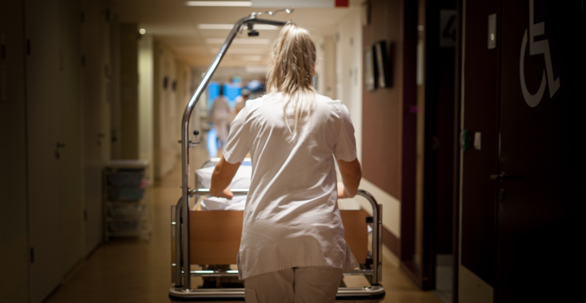 Verpleegkundige en duwt een bed door de gang van een ziekenhuis