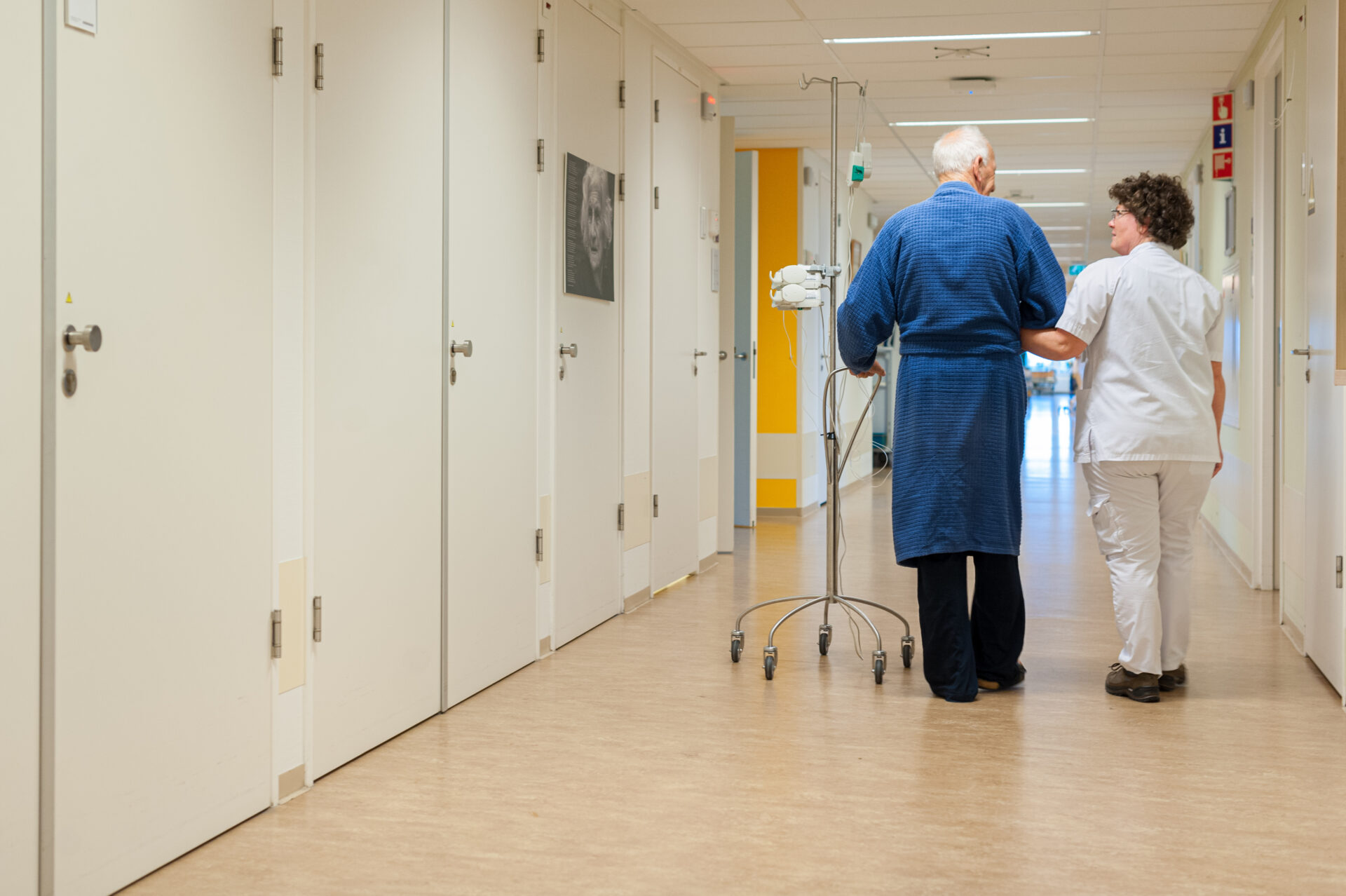Verpleegkundige met patient met dementie loopt over de gang.