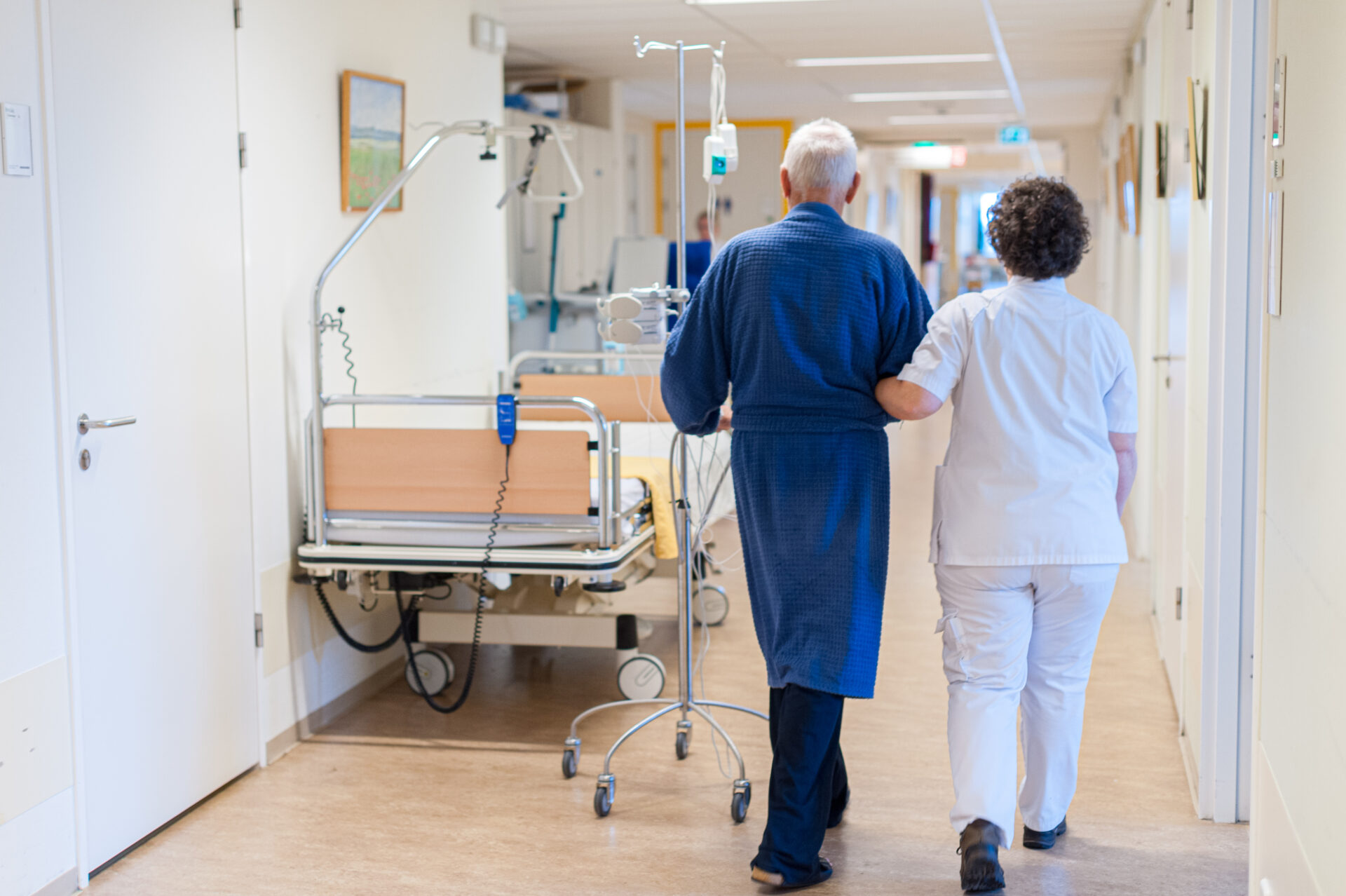 Een verpleegkundige en patient lopen arm in arm over de afdeling.