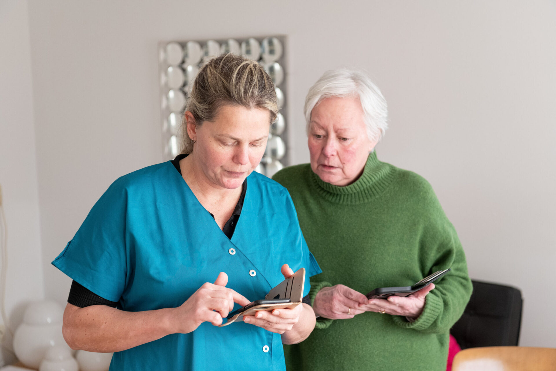 een verpleegkundige en een oudere client kijken op een mobiel.
