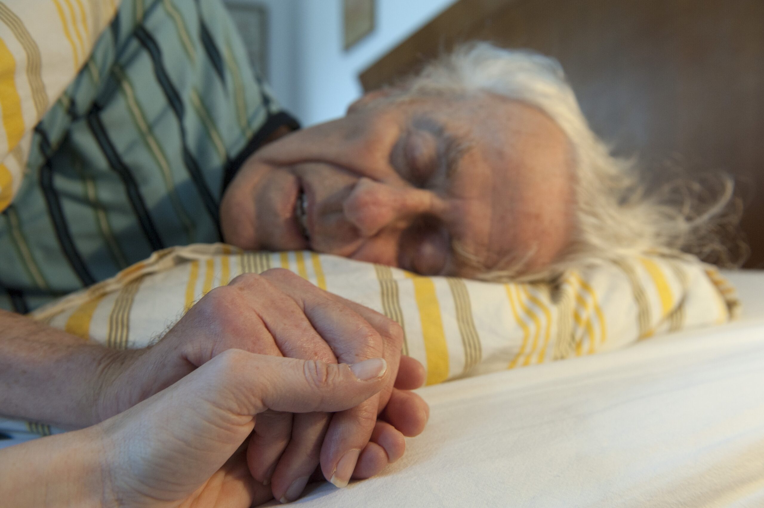 Naaste houdt hand vast van stervende cliënt in bed