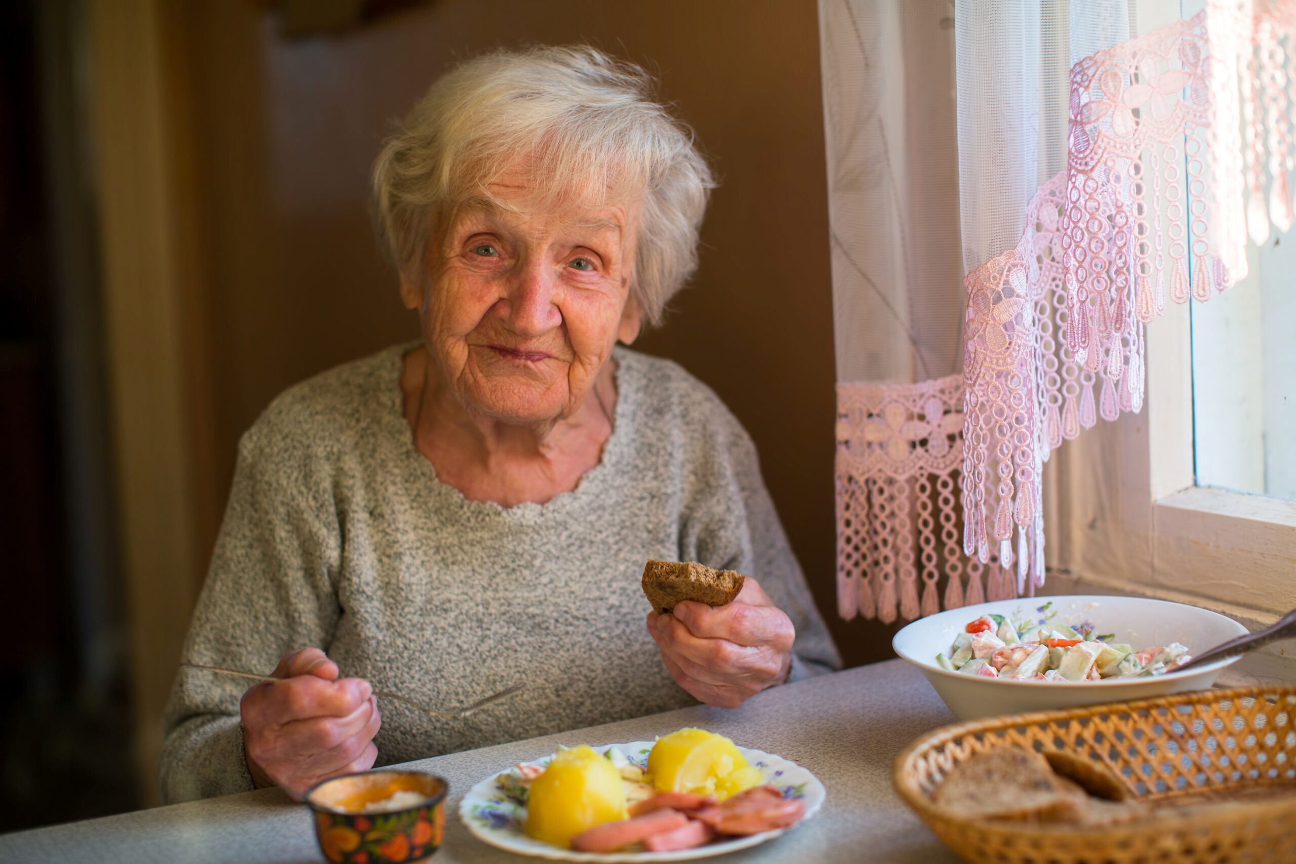 Oudere mevrouw eet maaltijd aan keukentafel thuis