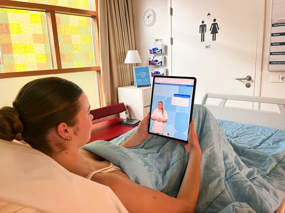 Vrouwelijke patiënt ligt in ziekenhuisbed met een tablet met daarop AVA de virtuele verpleegkundige.