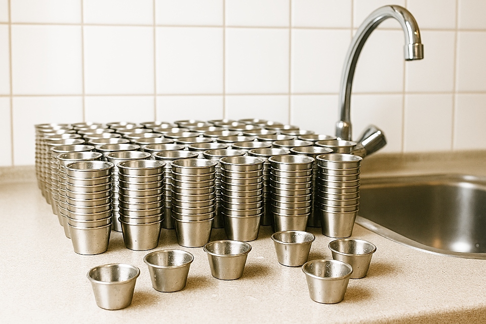 rvs-medicijncups op een aanrecht met daarnaast een kraan en wasbak.