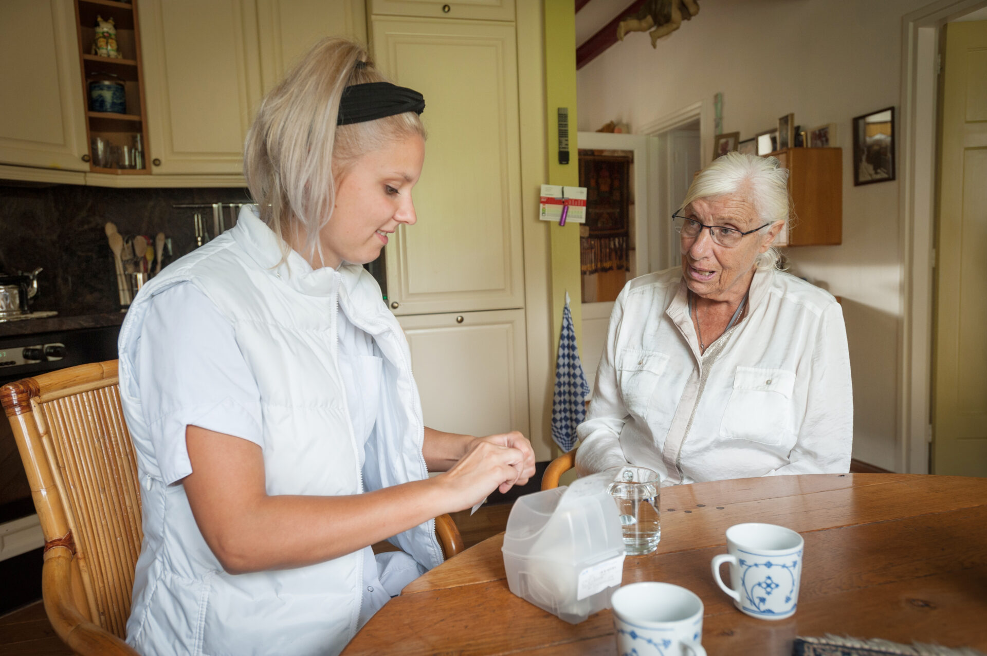 Jonge verpleegkundige geeft een client in de thuiszorg haar medicatie.