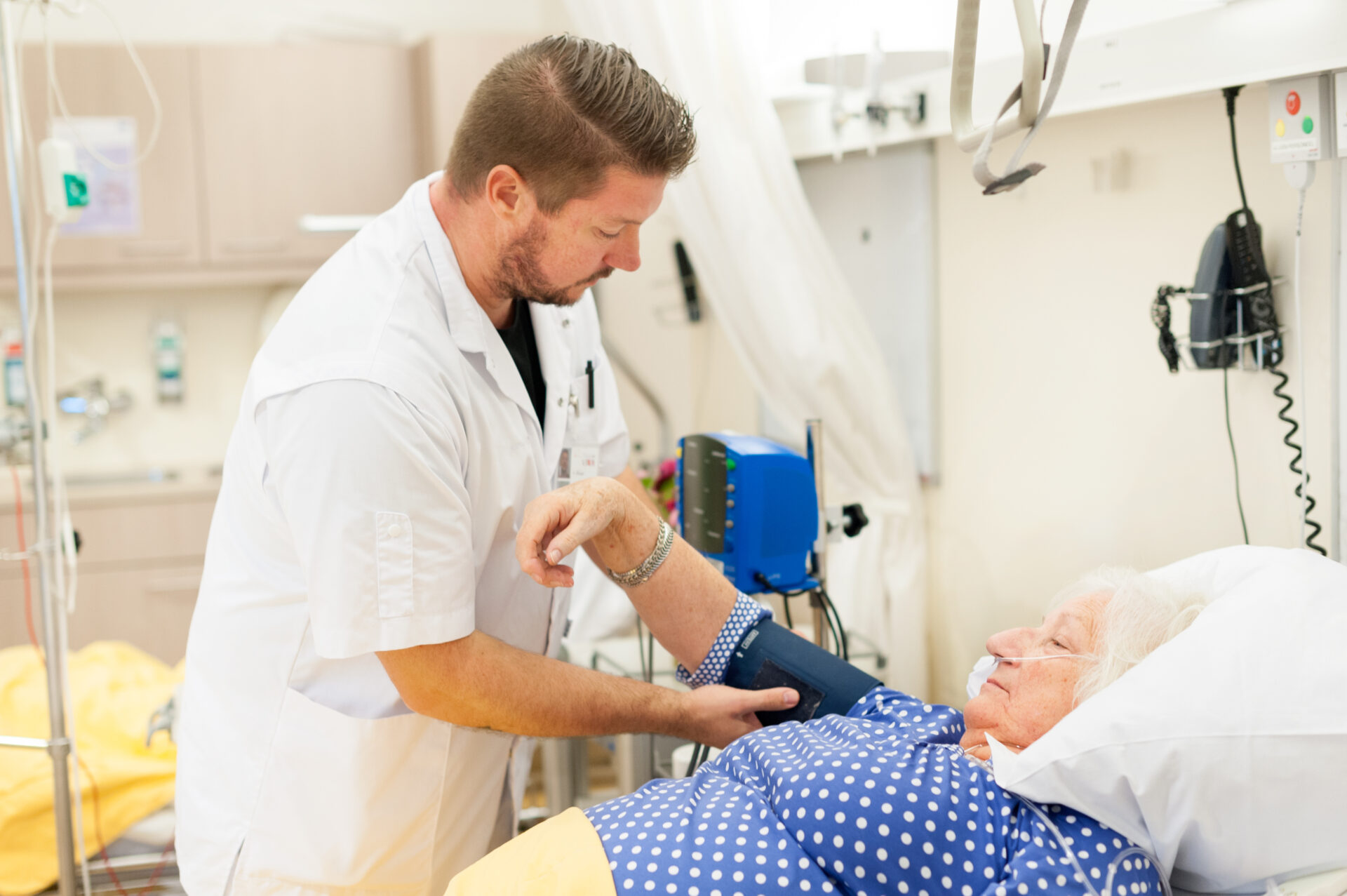 Een verpleegkundige meet de bloeddruk van een patiënt die in bed ligt.
