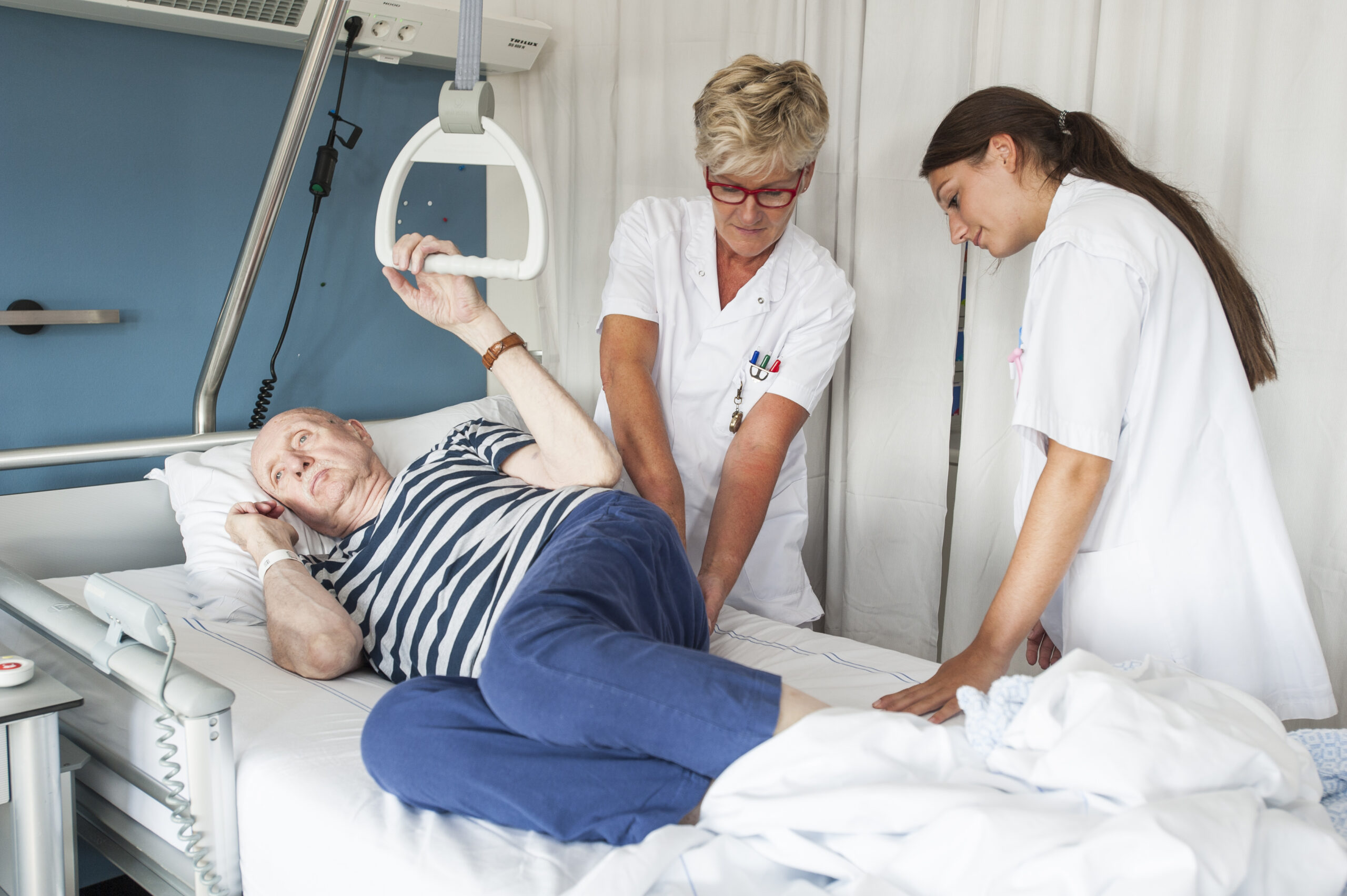 twee verpleegkundigen inspecteren de stuit van patiënt in ziekenhuisbed op signalen van decubitus