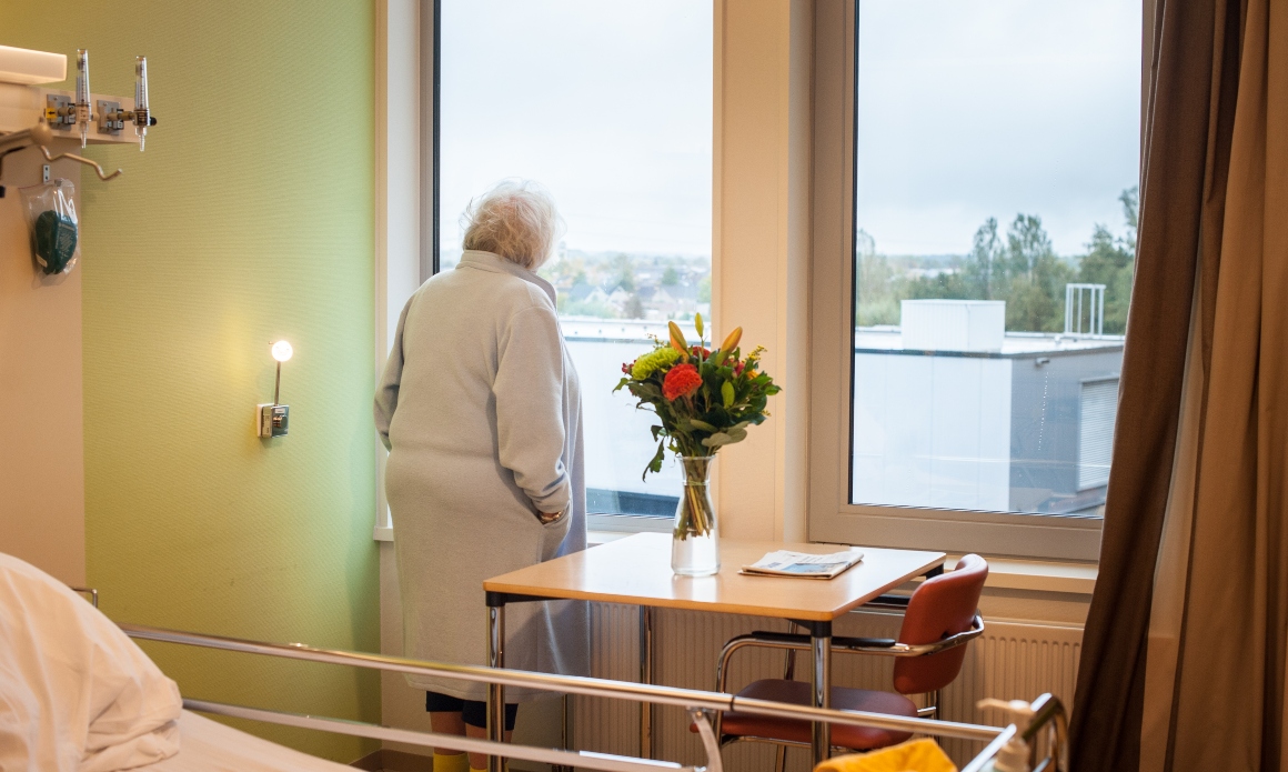 Oudere patiënt kijkt uit het raam van het ziekenhuis