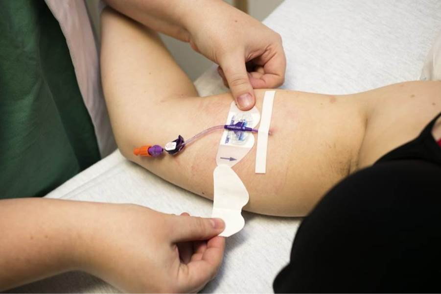 Een verpleegkundige vervangt de fixatiepleister van een PICC lijn.