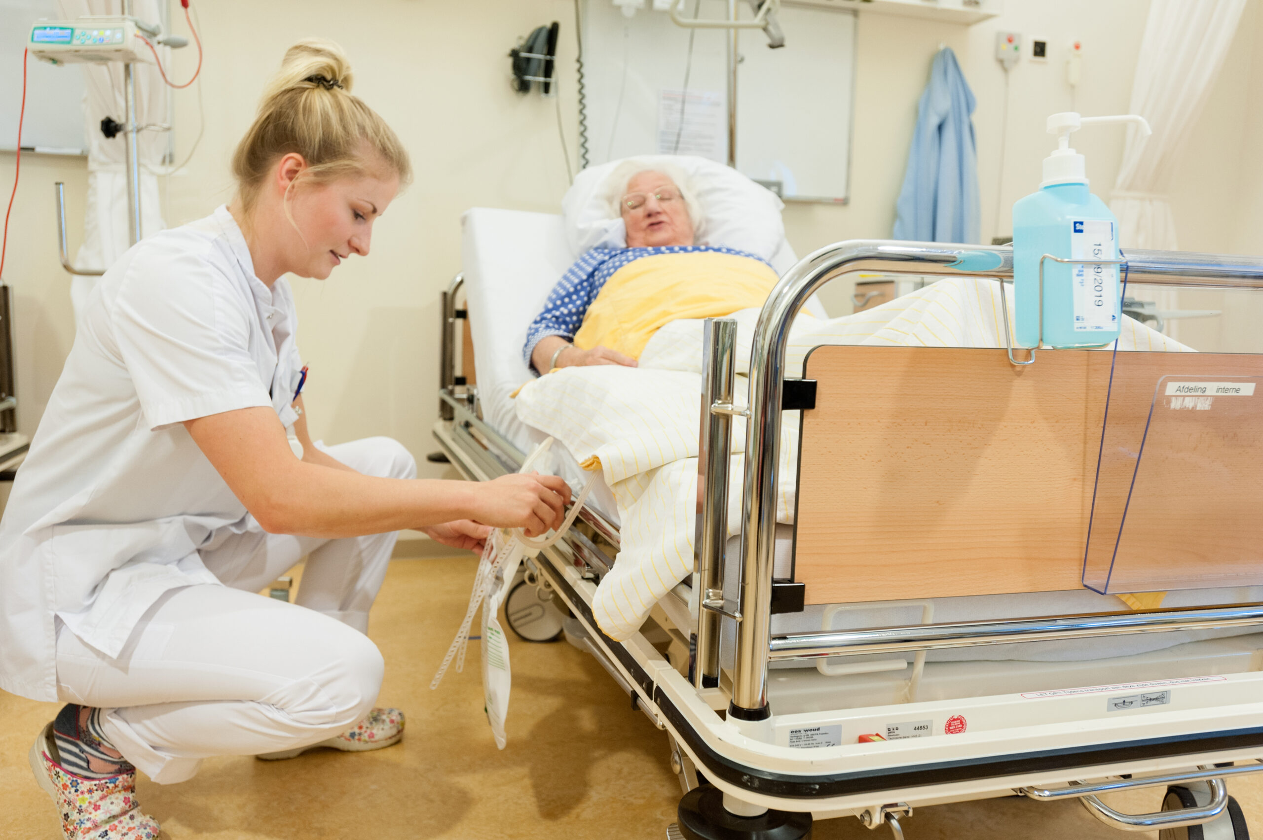 Verpleegkundige vervangt urinezak aan ziekenhuis bed.