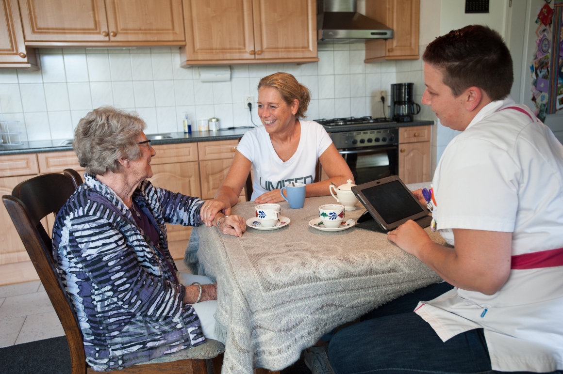 verpleegkundige in de wijk in gesprek met vrouwelijke zorgvrager en haar dochter die mantelzorger is.