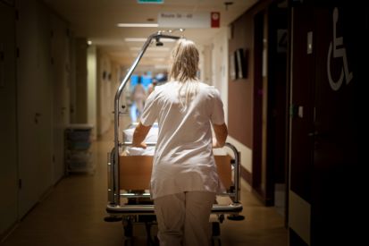 nachtdienst Verpleegkundige met nachtdienst loopt over de gang met een ziekenhuisbed