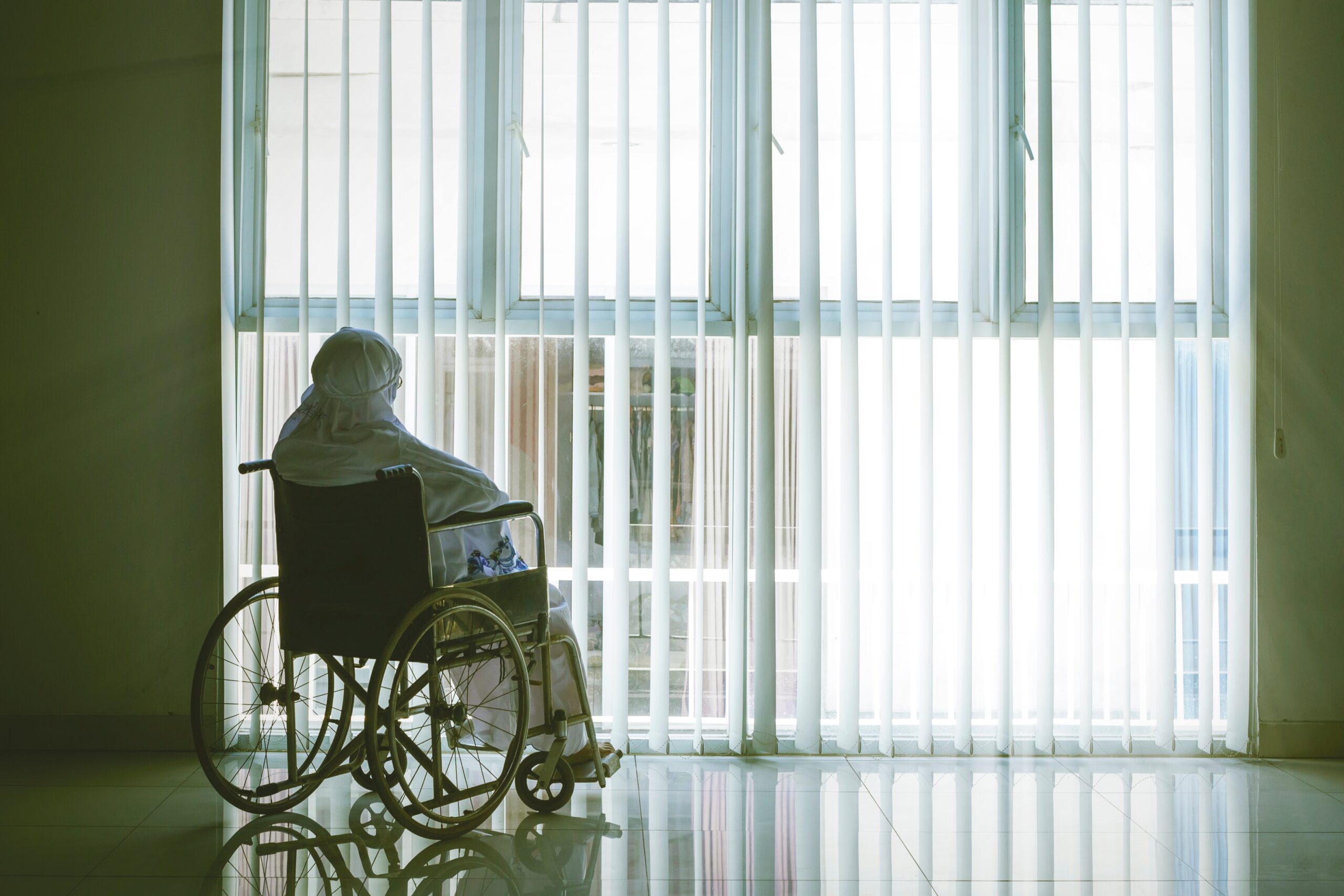 Vrouw met hoofddoek in rolstoel voor raam