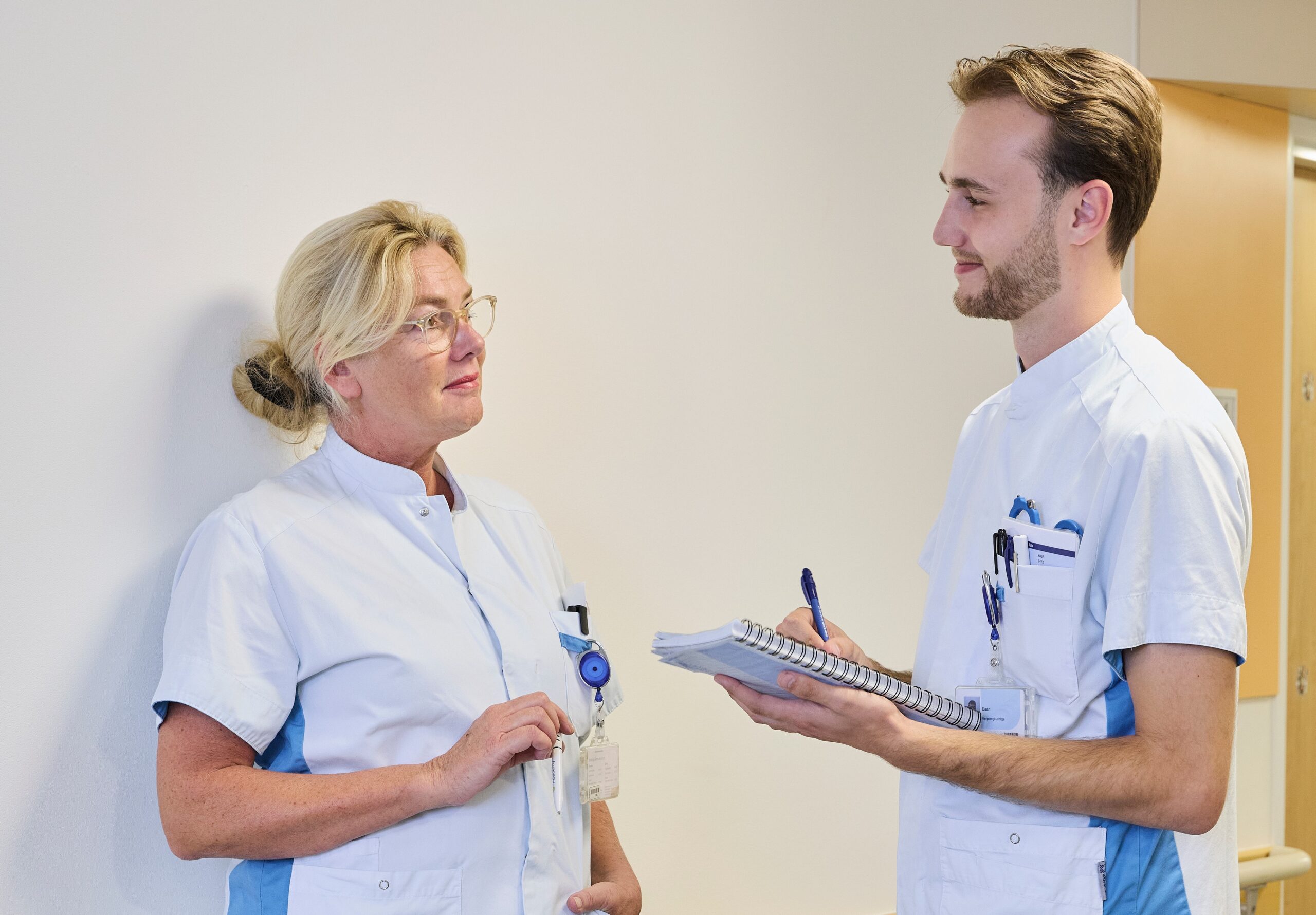 Twee verpleegkundigen zijn in overleg op de gang van de afdeling in een ziekenhuis.